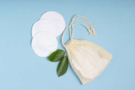 Cotton reusable make-up remover pads in a cloth bag and face wash and cleanser on a blue background. The concept of ecology and conscious consumption. Reusable cotton padsの写真素材
