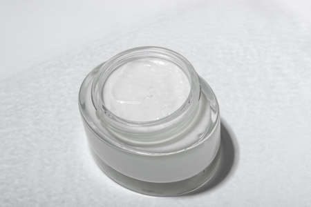 Cosmetic cream or mask in a glass jar with hard shadows from the leaves on a white background....