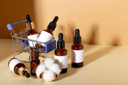 A set of cosmetic products with a dropper for facial skin care in a shopping trolley on a yellow background with shadows. The concept of buying cosmetics, online shoppingの写真素材