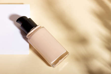 Foundation in a glass bottle on a background of geometric shapes. Facial corrector on a beige background with copy space. Packaging mockup with copy spaceの写真素材