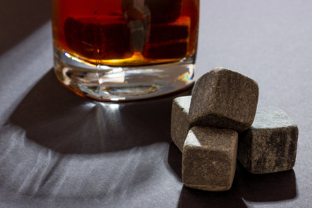 Transparent glass with whiskey on a dark background with bright rays of light. Whiskey stones in a glass glassの写真素材