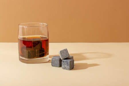 Transparent glass with whiskey on a dark background with bright rays of light. Whiskey stones in a glass glassの写真素材