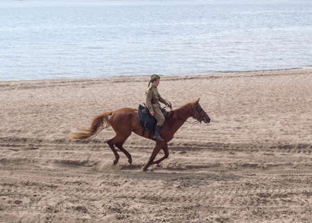 A dashing rider. A girl in military uniform rides a horse on the beach.の写真素材
