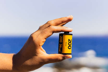 Unrecognizable brand 35mm film held in one hand against a summery, well lit background. Analog photography concept.の写真素材