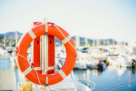Red lifebuoy photographed up close on a sunny day with a boat harbor and small boats in the background.の写真素材