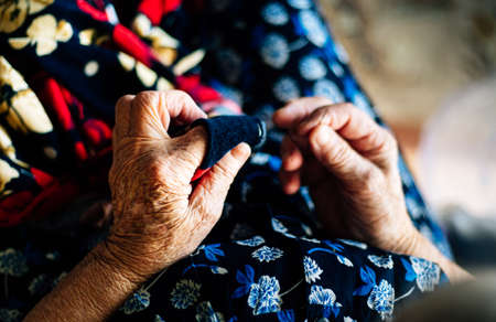 Hands of an elderly woman sewing a red garment seen from close up, very detailed. Concept of old age and something handmade.の写真素材
