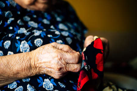 Hands of an elderly woman sewing a red garment seen from close up, very detailed. Concept of old age and something handmade.の写真素材