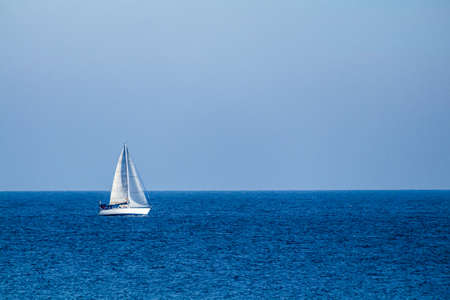 A white sailboat in the middle of the calm sea and under a wide clear blue sky.の写真素材
