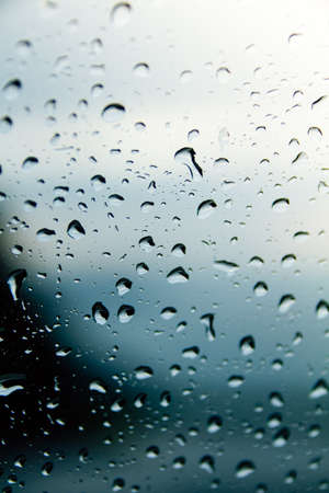 Raindrops on a window seen from close up. Cloudy and bluish day, nice background, could be used as a wallpaperの写真素材
