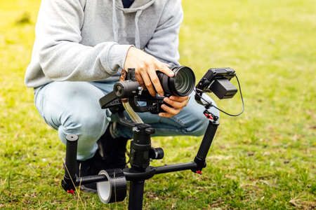 Camera operator adjusting the automatic camera stabilizer on a green lawn. Creation of videos with steadicam.の写真素材