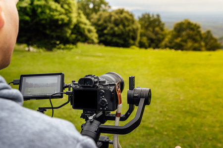 Stabilized camera on a gimbal / steadicam recording a scene. Photograph taken from behind and up close while the operator operates the camera.の写真素材