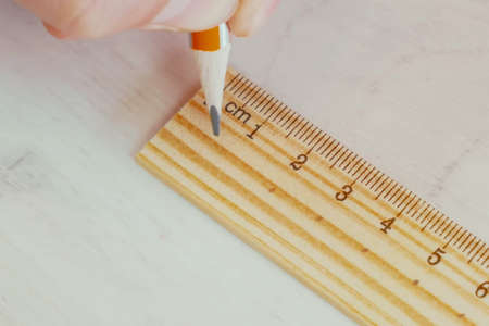A close-up hand holding a pencil and ruler while drawing.