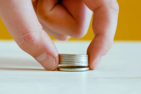 Hand picks up a stack of coins close-up lying on a white table.