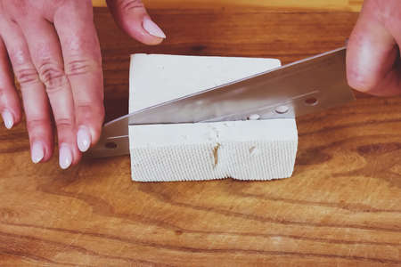 A hand holds a knife on a cutting board and cuts the cheese.