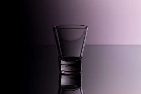 glass for vodka on glass bar counter, empty shot glass on purple background in nightclubの写真素材