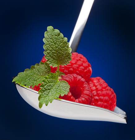 Raspberries on spoon with mint leaves on blue background. Macro photography artの写真素材