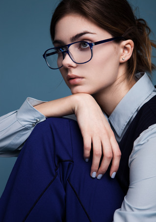 Businesswoman portrait with glasses and blue suit.Holding her own arm under the chin. Shot in studio on blue background.の写真素材