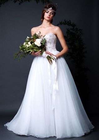 Young bride woman in wedding dress on grey background in the studio holding flowers with make up and hairstyleの写真素材