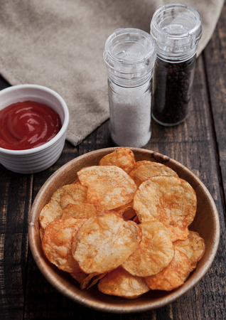 Bowl with potato crisps chips on wooden board. Salt and pepper on backgroundの写真素材