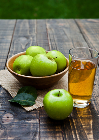 Apple juice glass with healthy green apples in wooden bowl. Outside in gardenの写真素材