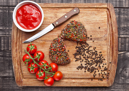 Beef raw steak with pepper and tomatoes on wooden board and  wooden background with ketchupの写真素材