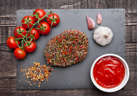 Beef raw steak with pepper and tomatoes on stone board and  wooden background with ketchupの写真素材