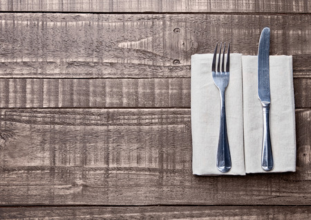 Knife and fork inside kitchen towel on wooden board. Place for textの写真素材