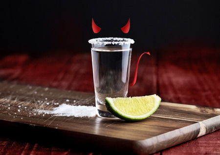 Tequila silver shot with lime slice devil colors on grunge wooden boardの写真素材