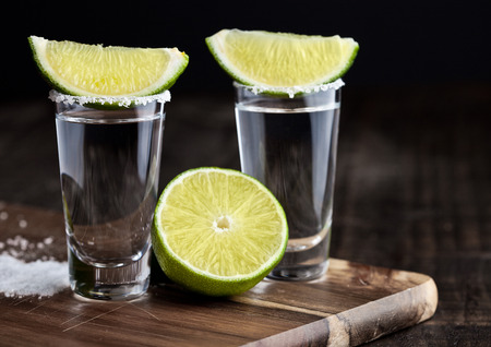 Tequila silver shots with lime slices and salt on grunge wooden boardの写真素材