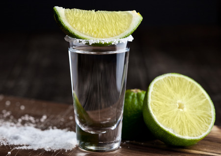 Tequila silver shot with lime slices and salt on grunge wooden boardの写真素材