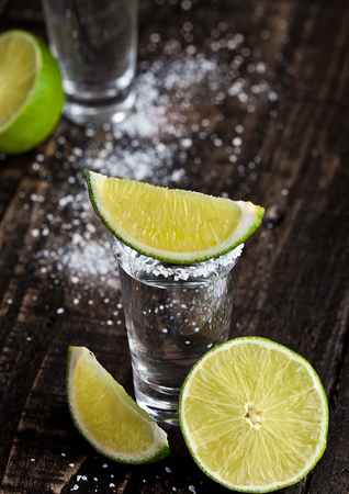 Tequila silver shot with lime slices and salt on grunge wooden boardの写真素材