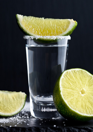 Tequila silver shot with lime slices and salt on grunge wooden boardの写真素材