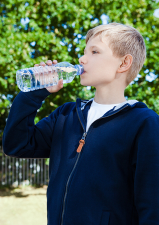 Young teenage boy drinking healthy still water in park summer timeの写真素材
