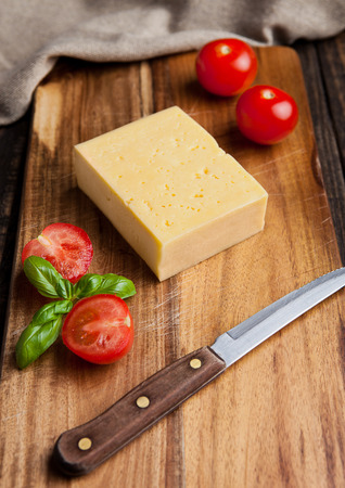 Cheese with tomatoes and basil on wooden cutting board with knifeの写真素材