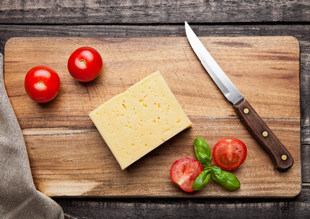 Cheese with tomatoes and basil on wooden cutting board with knifeの写真素材