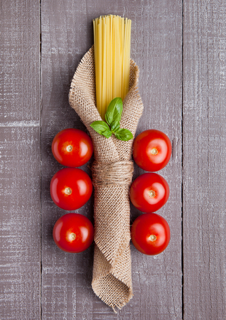 Raw spaghetti in linen cloth with tomatoes and basil on wooden tableの写真素材