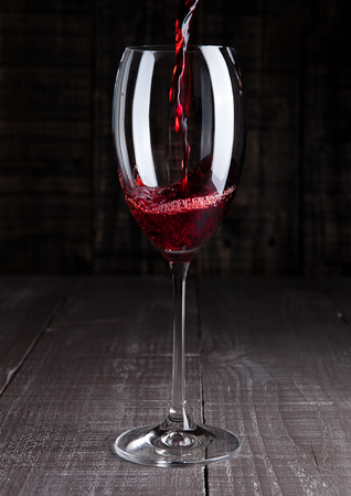 Pouring red wine from bottle to the glass on wooden boardの写真素材