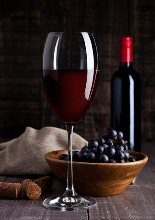Bottle and glass of red wine with grapes in bowl on wooden board backgroundの写真素材