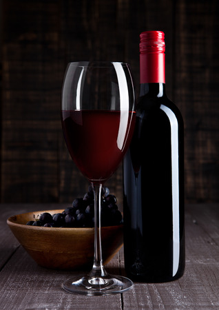 Bottle and glass of red wine with grapes in bowl on wooden board backgroundの写真素材