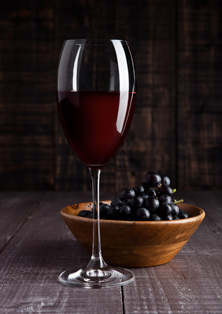 Glass of red wine with grapes in bowl on wooden board backgroundの写真素材