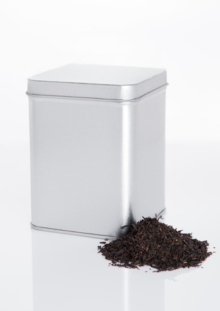 Black tea steel jar with loose tea next to it on white backgroundの写真素材
