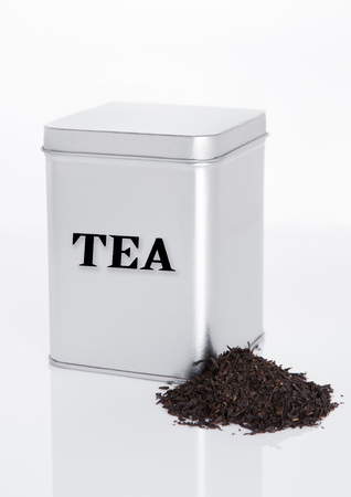 Black tea steel jar with loose tea next to it on white backgroundの写真素材