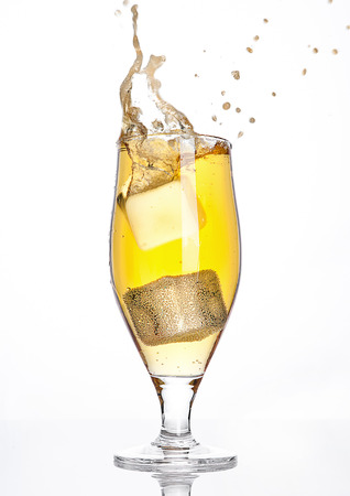 Glass of beer cider with ice cube splash on white backgroundの写真素材