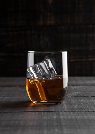 Glass of whiskey with ice cubes on wooden backgroundの写真素材