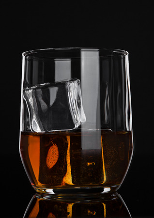 Glass of whiskey with ice cubes on wooden backgroundの写真素材