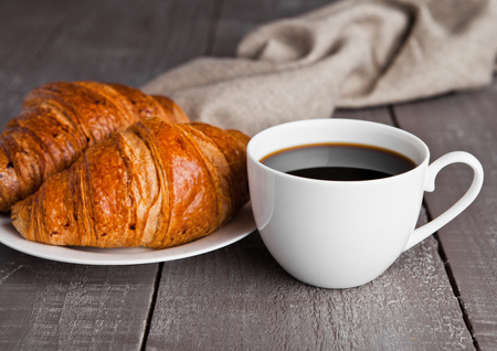 Cup of black coffee and croissant for breakfast on wooden backgroundの写真素材