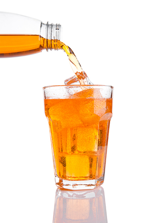 Pouring orange energy soda drink in glass with ice on white backgroundの写真素材
