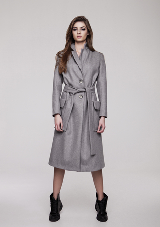 Beautiful young girl wearing long grey jacket on grey backgroundの写真素材