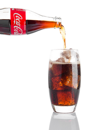 LONDON, UK - NOVEMBER 07, 2016: Classic bottle Of Coca-Cola pouring in glass and ice cubes on white backgroundのeditorial素材