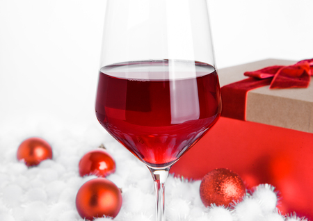 Glass of red wine on snow with christmas balls on white backgroundの写真素材